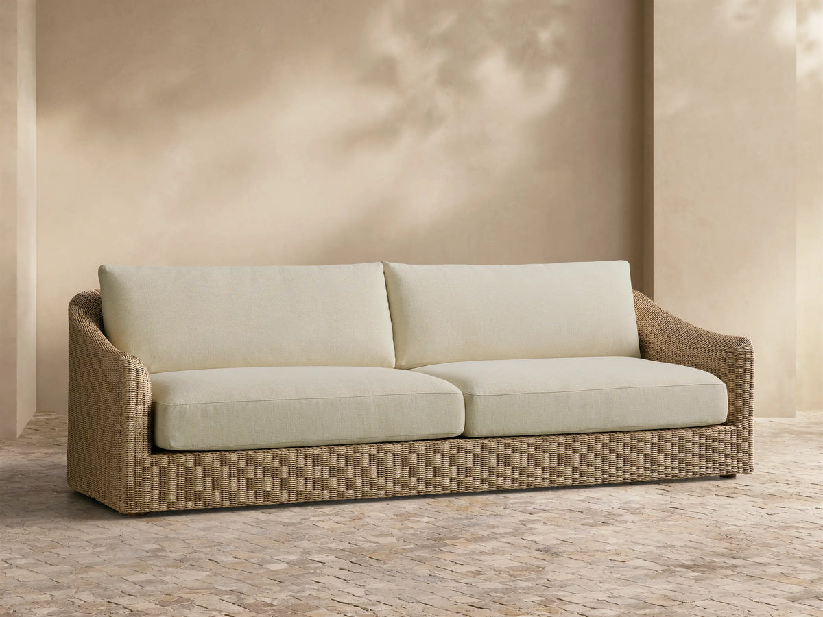 Front view of the Ancona Outdoor Sofa with natural-toned woven wicker and cream cushions.