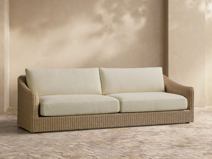 Front view of the Ancona Outdoor Sofa with natural-toned woven wicker and cream cushions.