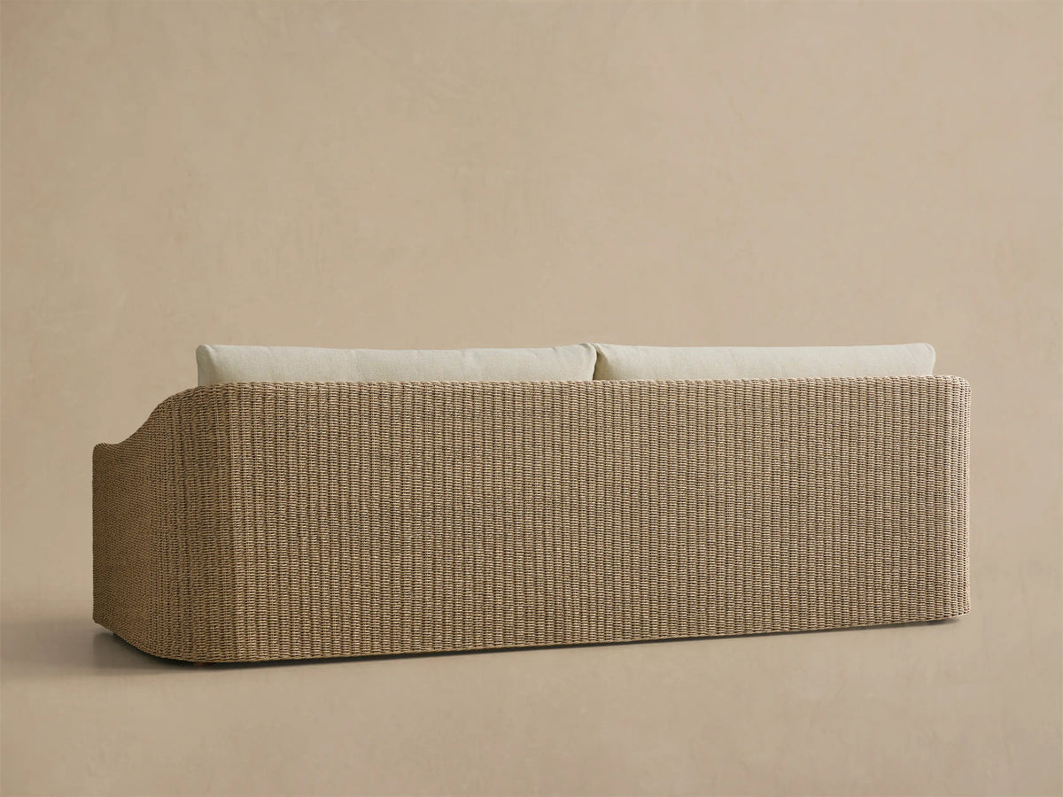 Close-up of the Ancona Outdoor Sofa, featuring light beige cushions and a natural woven wicker frame with a curved armrest.