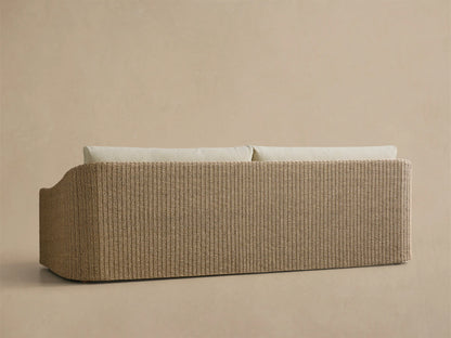 Close-up of the Ancona Outdoor Sofa, featuring light beige cushions and a natural woven wicker frame with a curved armrest.