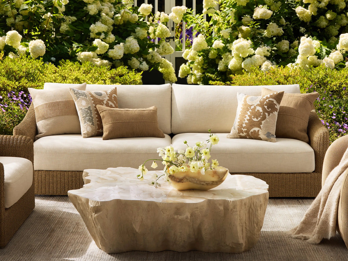 Rear and side view of the beige woven Ancona Outdoor Sofa with light cream cushions.