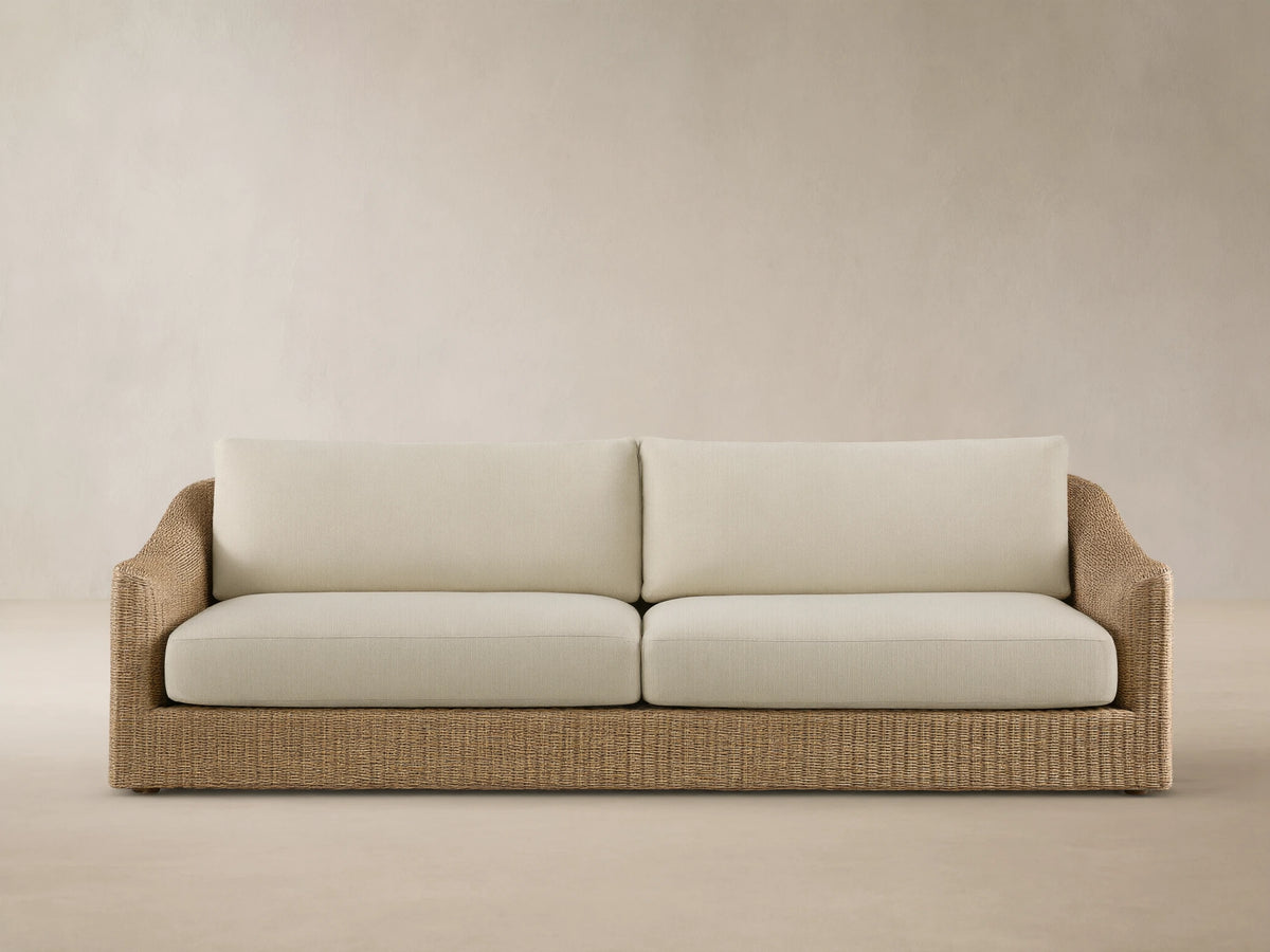 Front view of the Ancona Outdoor Sofa with natural-toned woven wicker and cream cushions.