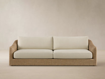 Front view of the Ancona Outdoor Sofa with natural-toned woven wicker and cream cushions.