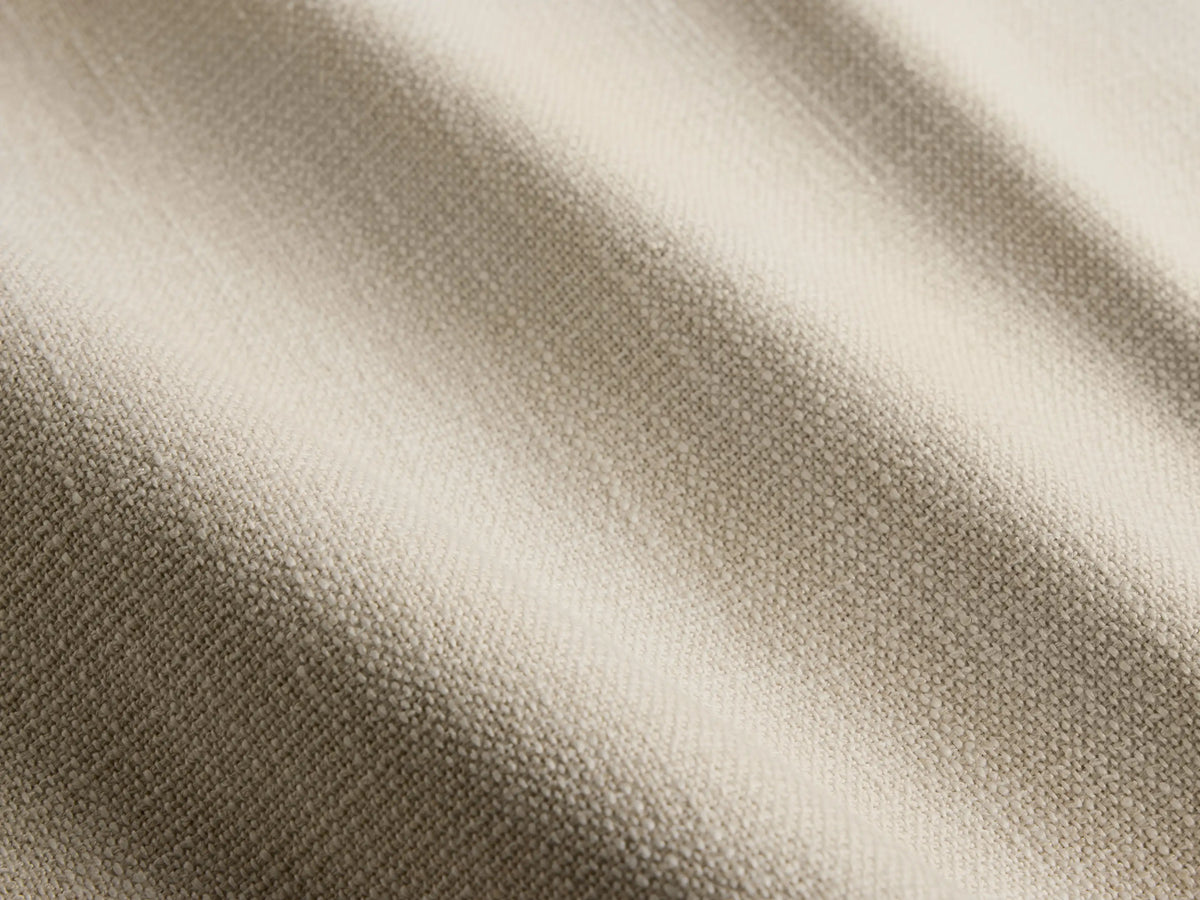 Close-up of the Ancona Outdoor Sofa, showing light beige cushions and a natural brown handwoven wicker frame with a curved armrest.