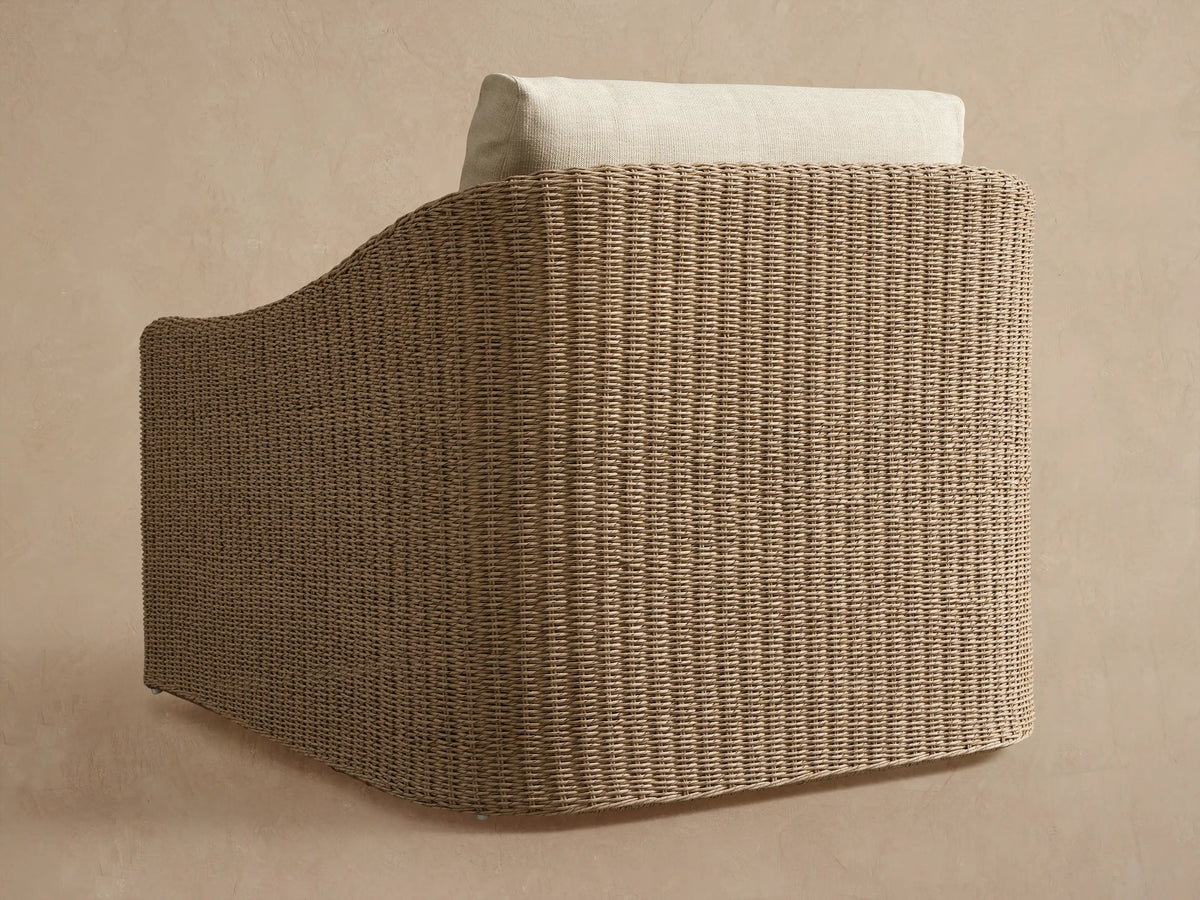 Side view of Ancona Outdoor Swivel Chair with light beige handwoven wicker and a cream back cushion.