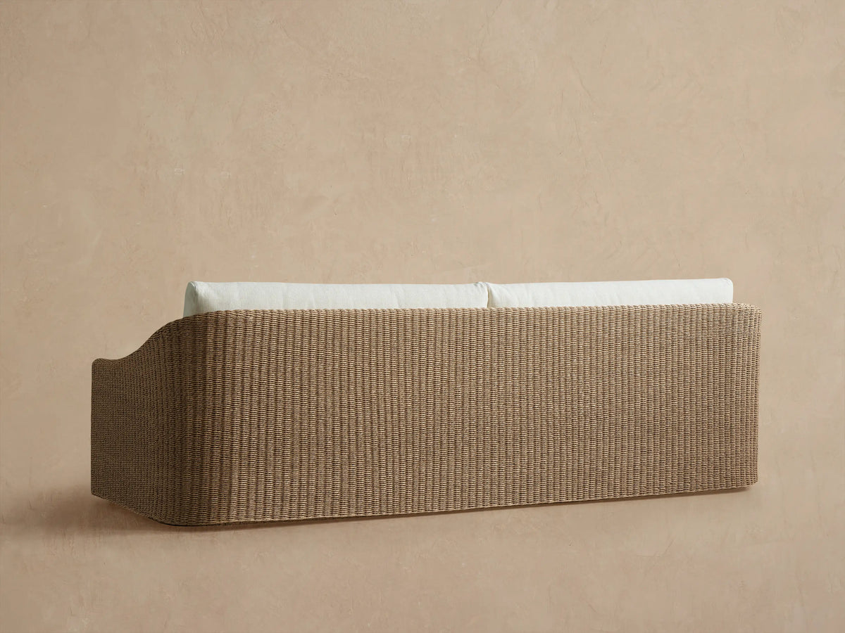 Ancona Outdoor Sofa close-up. Light brown handwoven wicker armrest with plush off-white seat and back cushions.