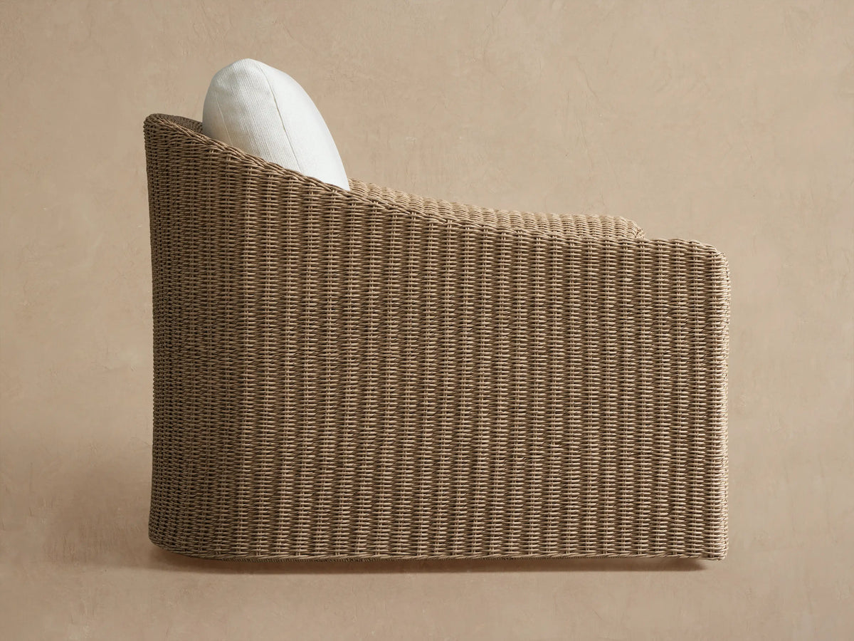 Ancona Outdoor Swivel Chair, back view. Curved brown all-weather wicker with a white cushion, against a light tan background.