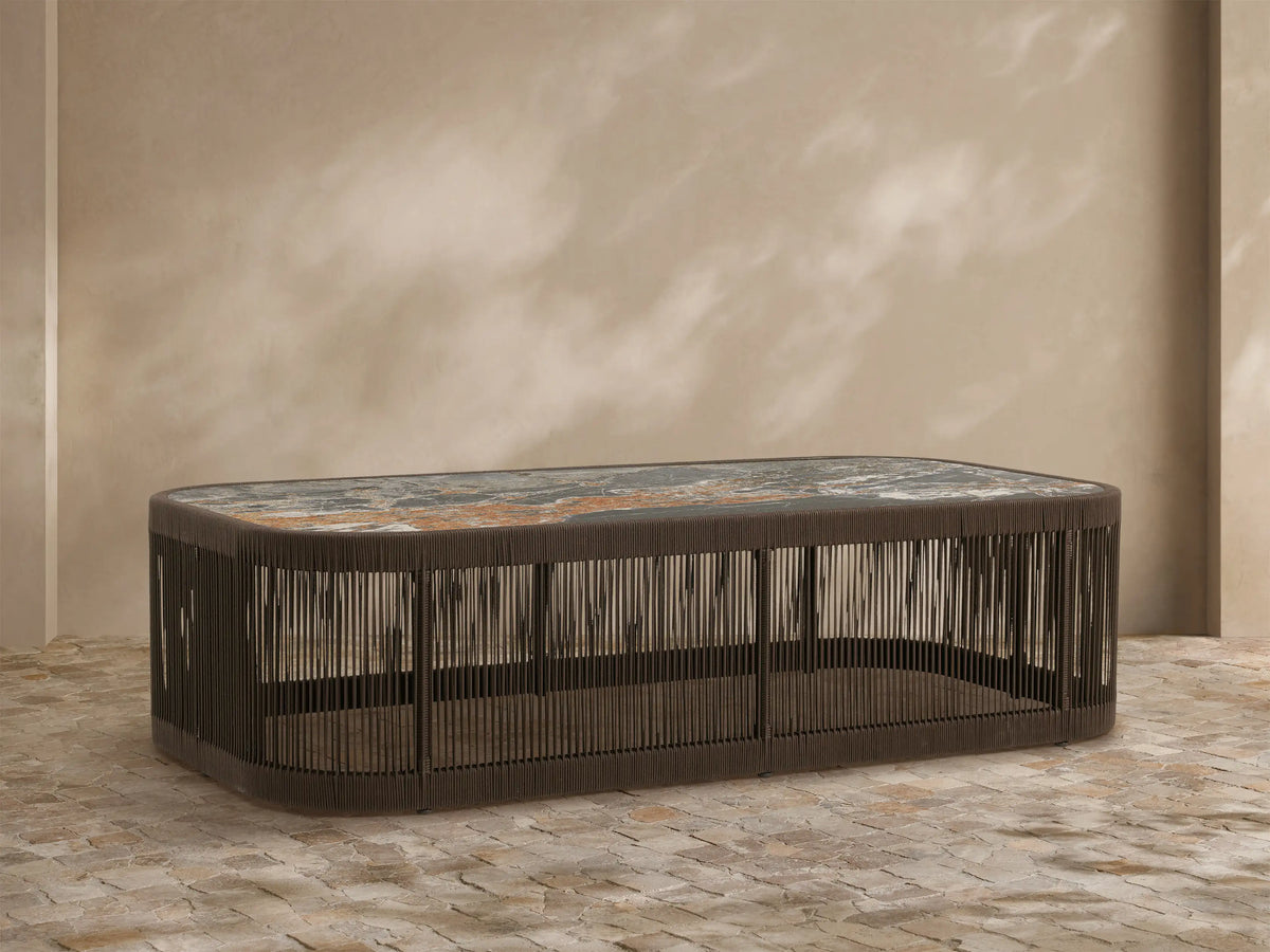 Anzio Outdoor Coffee Table: Low dark brown handwoven rope base, rectangular mottled gray & rust sintered stone top on patio.