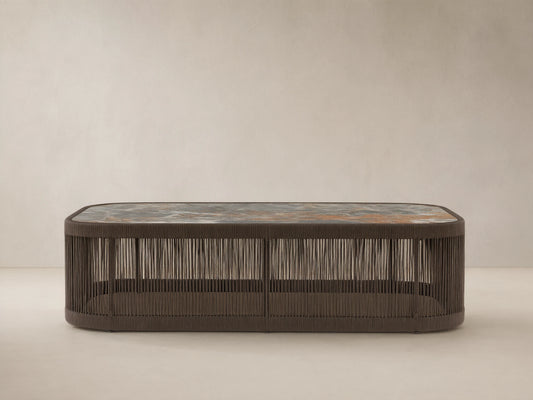 Anzio Outdoor Coffee Table: Low dark brown handwoven rope base, rectangular mottled gray & rust sintered stone top on patio.