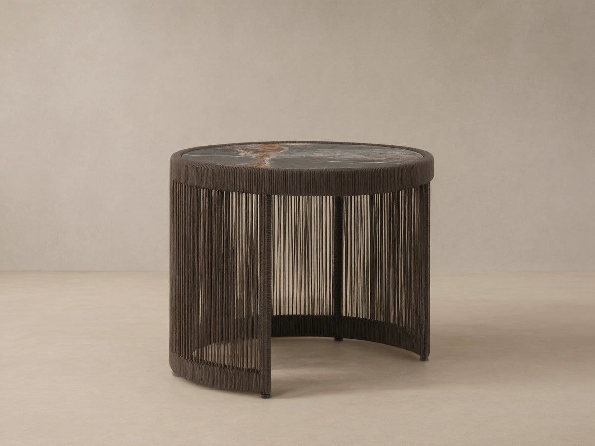 Round Anzio Outdoor Nesting End Table with a dark woven rope base and a mottled gray sintered stone top on a patio.