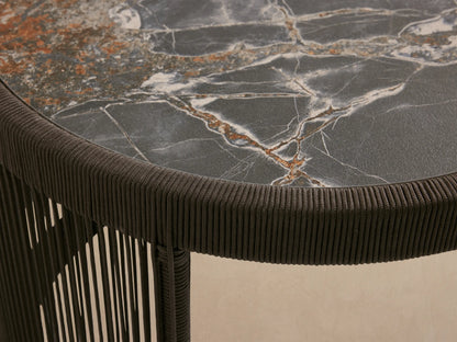 Cylindrical Anzio Outdoor Nesting End Table, mottled stone top, dark brown woven rope sides with vertical linear pattern, on patio.