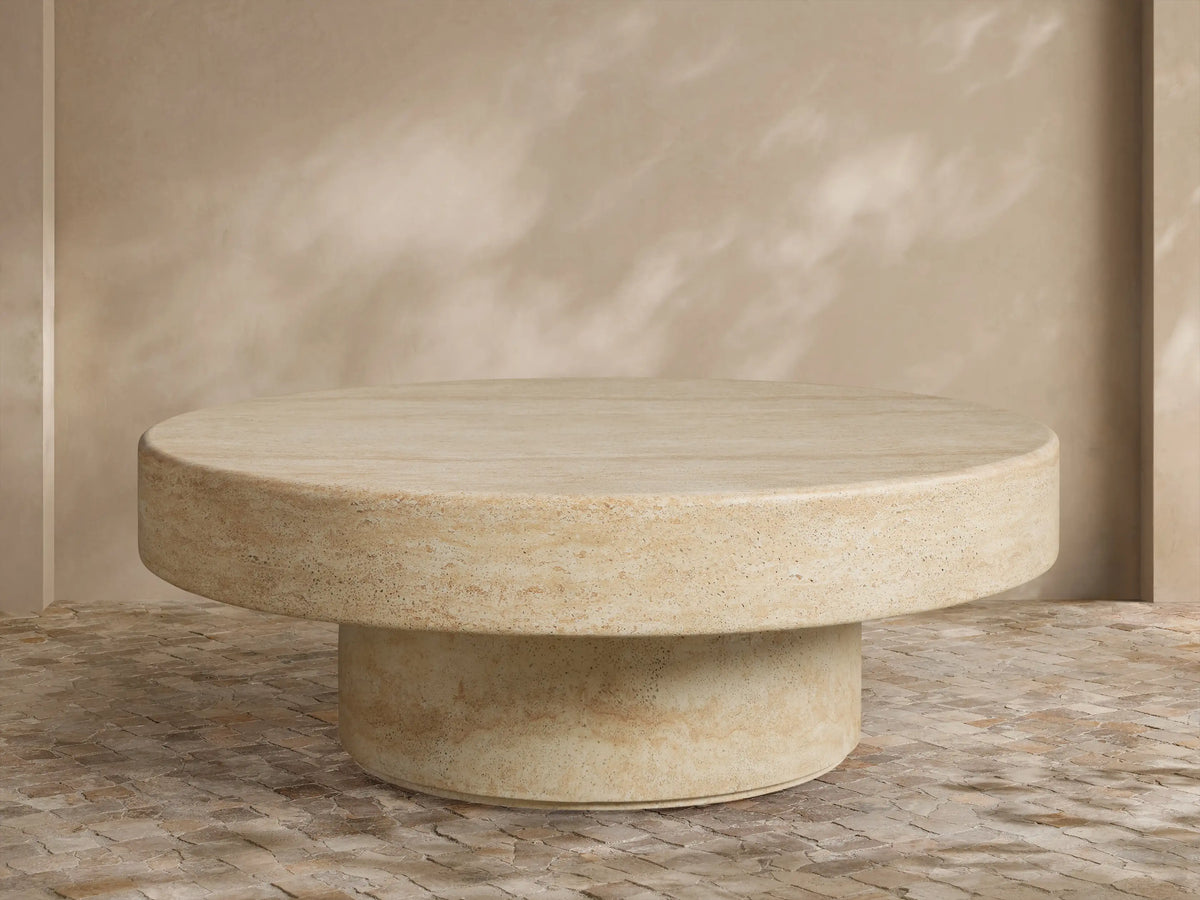 Azores Outdoor Round Coffee Table, round light beige faux travertine, shown on a light brown patterned tile floor.