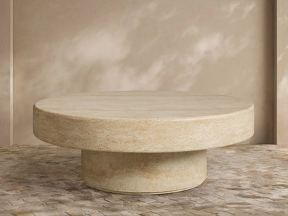 Azores Outdoor Round Coffee Table, round light beige faux travertine, shown on a light brown patterned tile floor.