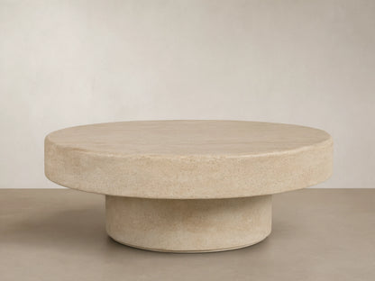 Azores Outdoor Round Coffee Table, round light beige faux travertine, shown on a light brown patterned tile floor.
