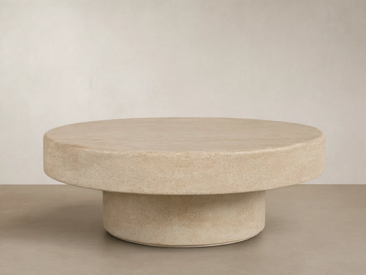 Azores Outdoor Round Coffee Table, round light beige faux travertine, shown on a light brown patterned tile floor.
