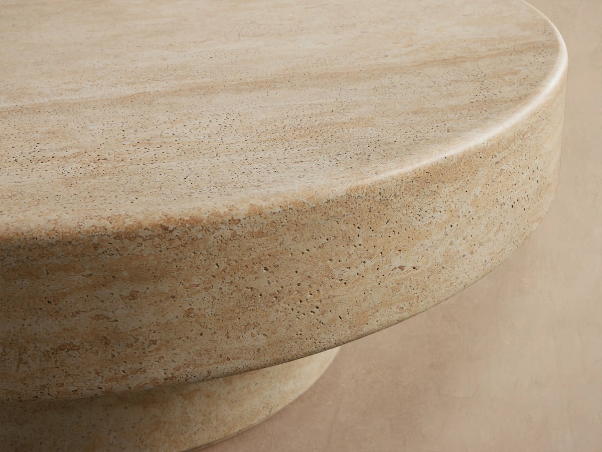Azores Outdoor Round Coffee Table, round light beige faux travertine, shown on a light brown patterned tile floor.