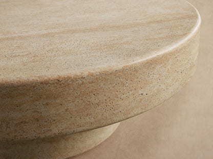 Azores Outdoor Round Coffee Table, round light beige faux travertine, shown on a light brown patterned tile floor.