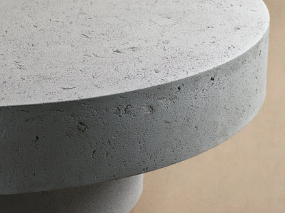 Faux travertine Azores Outdoor Round Coffee Table with a smooth round top and cylindrical base, styled in an outdoor patio setting.