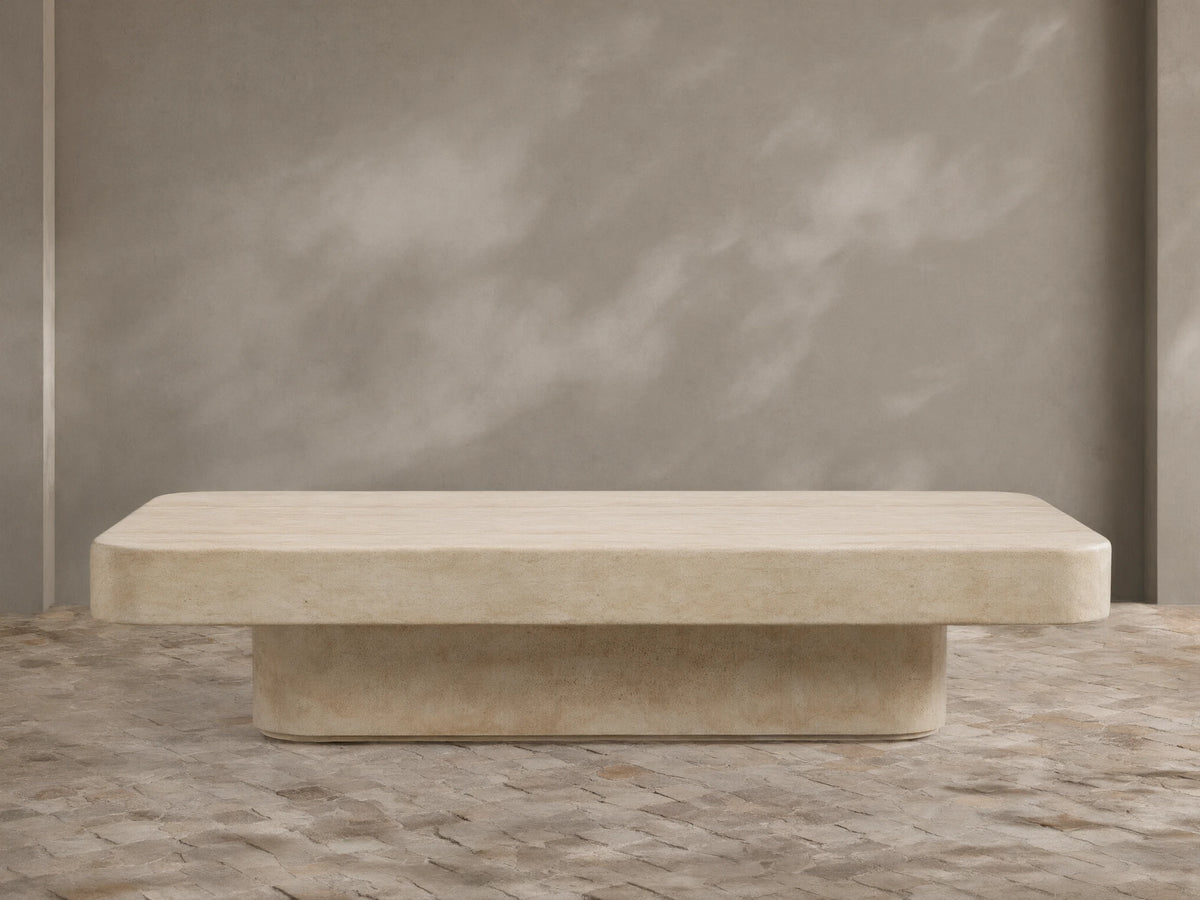 Azores Outdoor Coffee Table, light beige faux travertine with rounded rectangular top and base, on a textured stone floor.