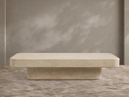 Azores Outdoor Coffee Table, light beige faux travertine with rounded rectangular top and base, on a textured stone floor.