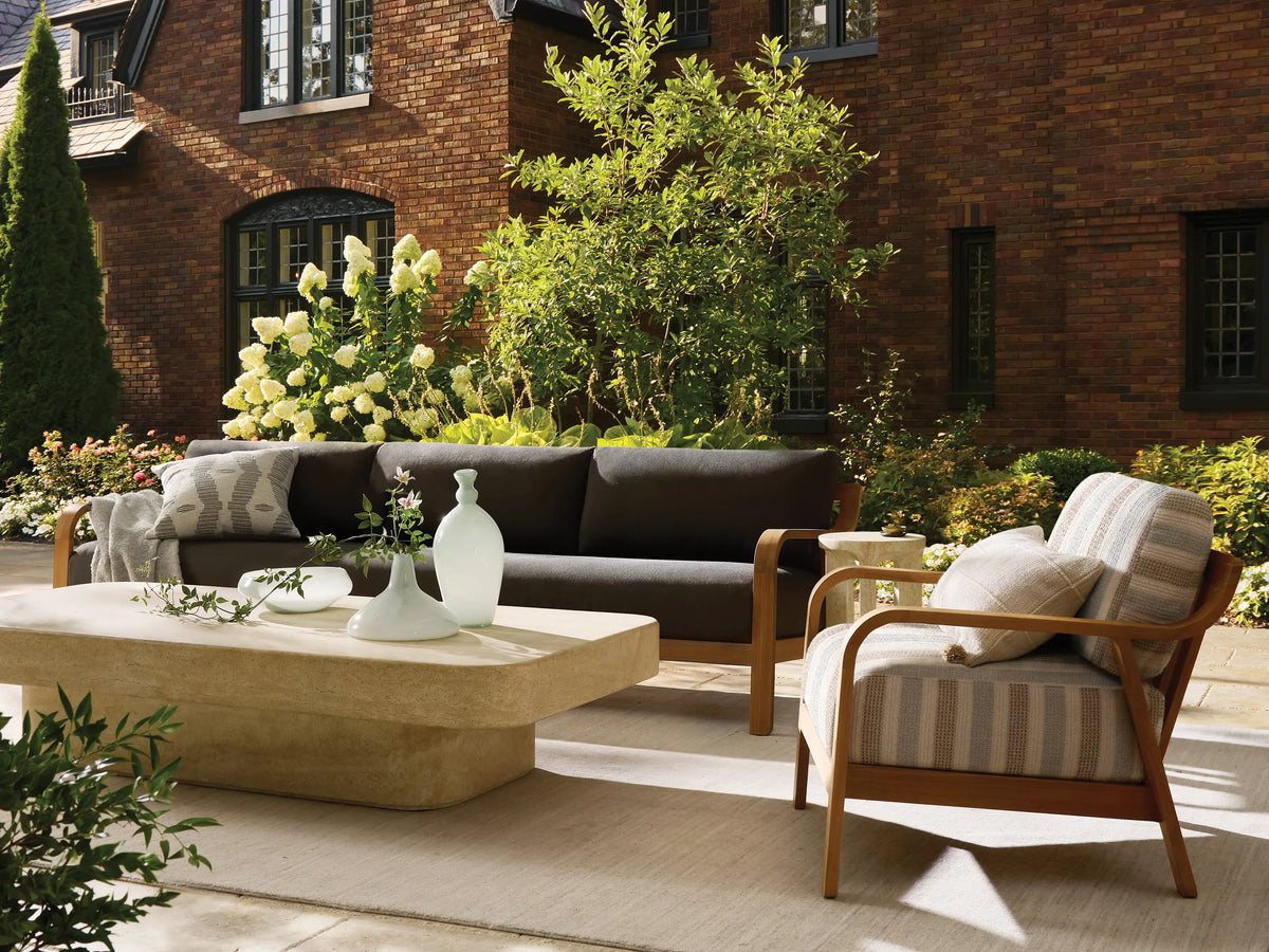 Azores Outdoor Coffee Table, light beige faux travertine with rounded rectangular top and base, on a textured stone floor.