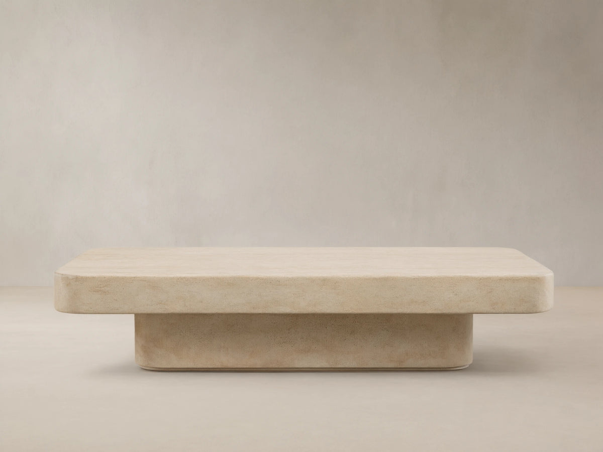 Azores Outdoor Coffee Table, light beige faux travertine with rounded rectangular top and base, on a textured stone floor.