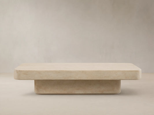 Azores Outdoor Coffee Table, light beige faux travertine with rounded rectangular top and base, on a textured stone floor.