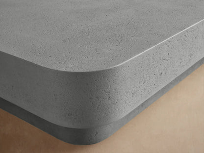 Azores Outdoor Coffee Table, light gray rectangular concrete-look table with rounded edges, on a low base, angled.