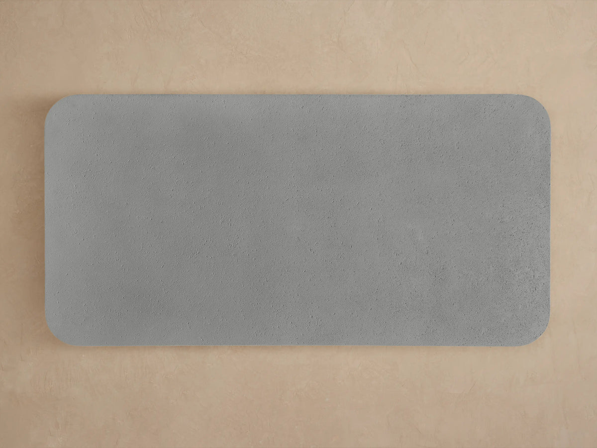Close-up of the Azores Outdoor Coffee Table's rounded gray concrete-like textured corner with a thick edge, against a beige background.