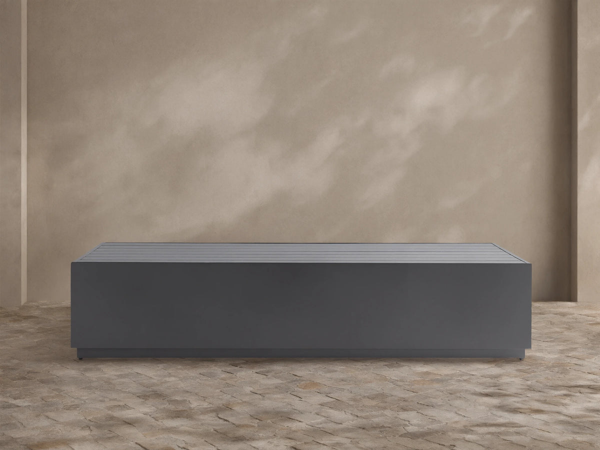 Dark gray, rectangular Bal Harbour Outdoor Aluminum Coffee Table with a slatted top, shown on a stone patio.