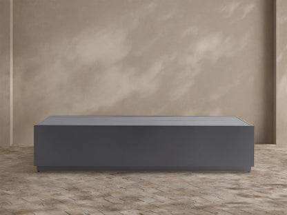 Dark gray, rectangular Bal Harbour Outdoor Aluminum Coffee Table with a slatted top, shown on a stone patio.