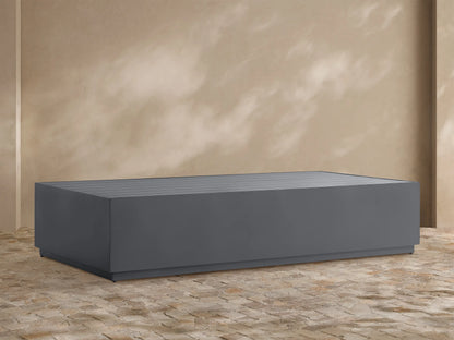 Dark gray, rectangular Bal Harbour Outdoor Aluminum Coffee Table with a slatted top, shown on a stone patio.