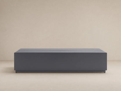 Dark gray, rectangular Bal Harbour Outdoor Aluminum Coffee Table with a slatted top, shown on a stone patio.