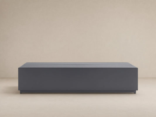Dark gray, rectangular Bal Harbour Outdoor Aluminum Coffee Table with a slatted top, shown on a stone patio.