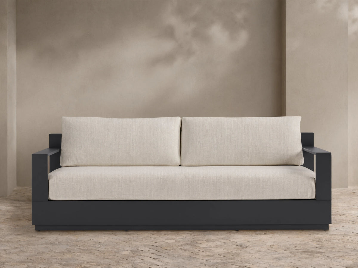 Bal Harbour Outdoor Aluminum Sofa with dark gray frame and light beige cushions, centered on a patio against a neutral wall.