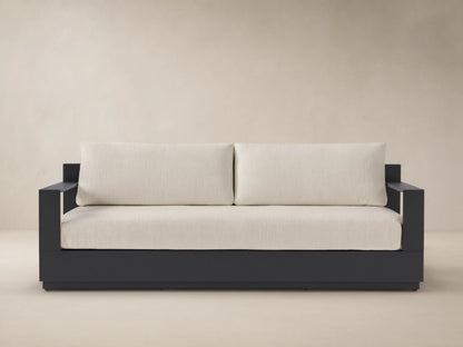 Bal Harbour Outdoor Aluminum Sofa with dark gray frame and light beige cushions, centered on a patio against a neutral wall.
