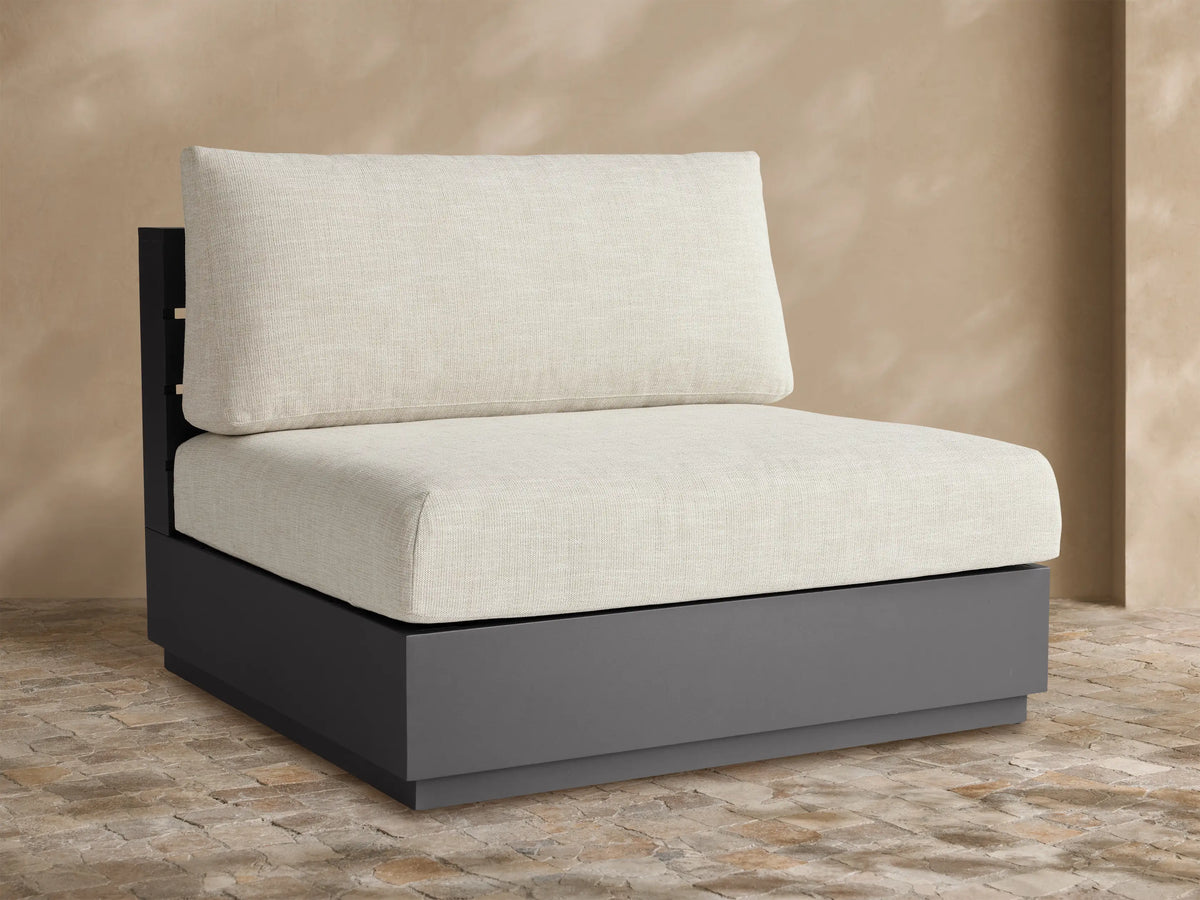 Bal Harbour armless chair with dark gray aluminum frame and light beige cushions, set on an outdoor patio.