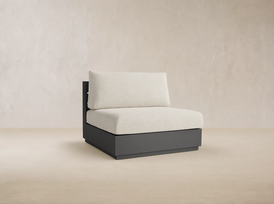 Bal Harbour armless chair with dark gray aluminum frame and light beige cushions, set on an outdoor patio.