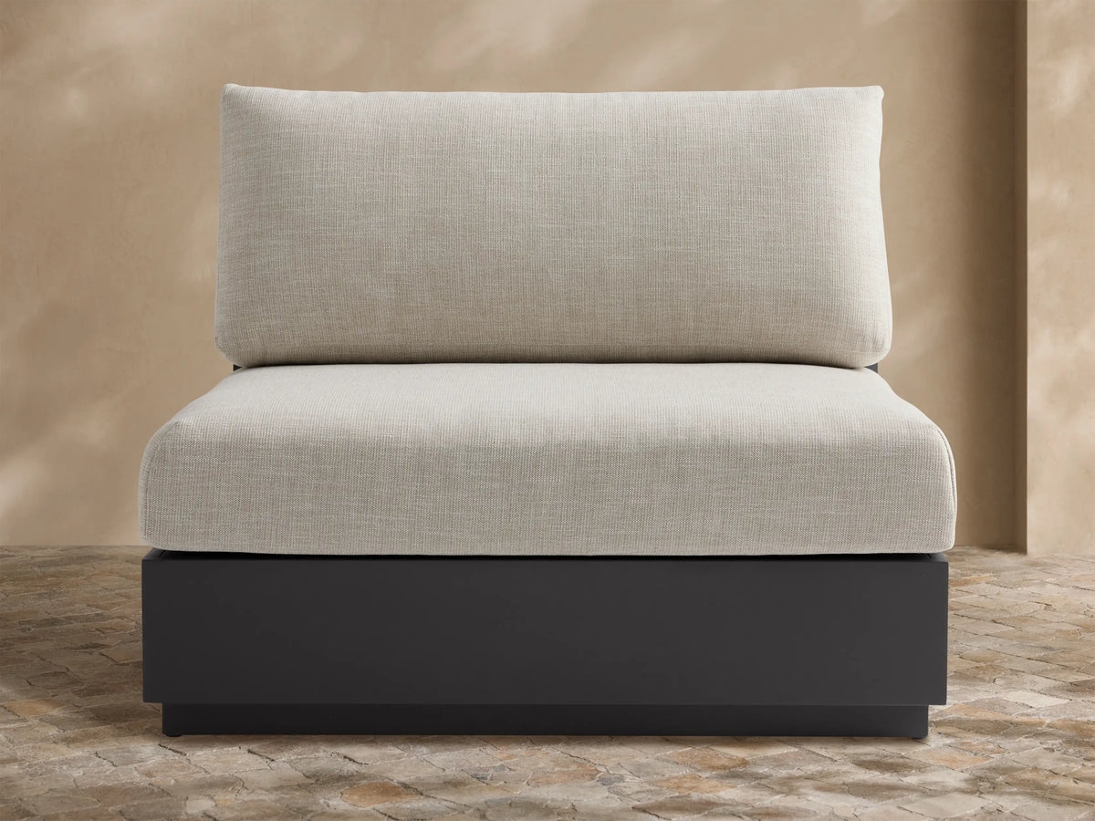 Bal Harbour armless chair with dark gray aluminum frame and light beige cushions, set on an outdoor patio.