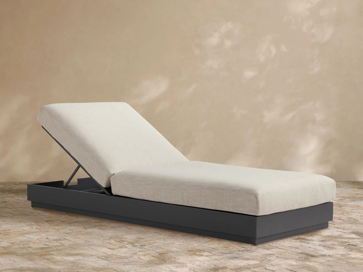 Bal Harbour Outdoor Aluminum Chaise with dark gray base and light beige cushion, raised backrest, on a tiled patio.
