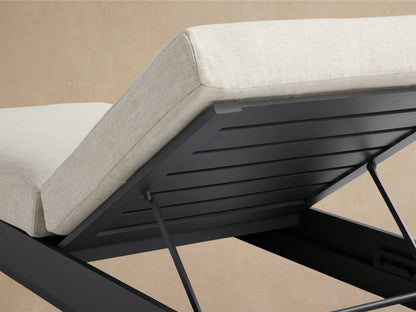 Bal Harbour Outdoor Aluminum Chaise with dark gray frame and light cream cushions. Backrest is elevated, side view against a warm tan wall.