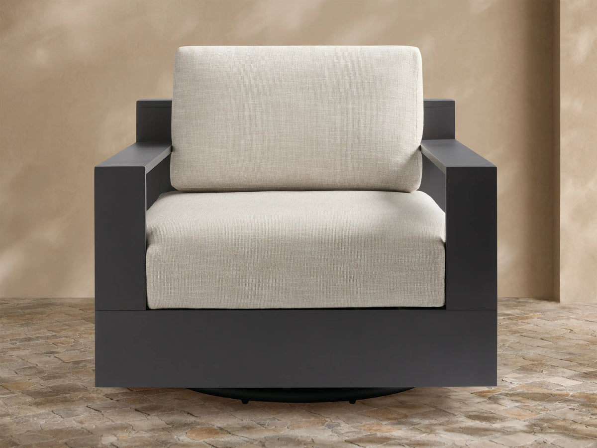 Front view of the Bal Harbour Outdoor Aluminum Swivel Chair with a dark gray frame and light beige cushions on an outdoor patio.