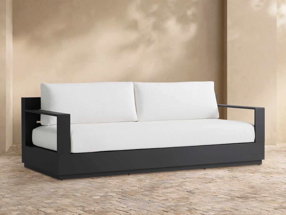 Outdoor scene with the Bal Harbour Outdoor Aluminum Sofa, featuring light cushions and a dark gray frame, styled with brown pillows and throws.