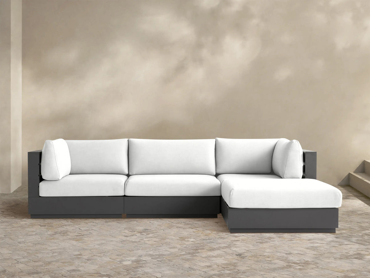 L-shaped Bal Harbour Outdoor Aluminum Four-Piece Sectional with dark gray frame & white cushions, on a stone patio.