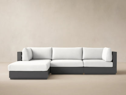 L-shaped Bal Harbour Outdoor Aluminum Four-Piece Sectional with dark gray frame & white cushions, on a stone patio.