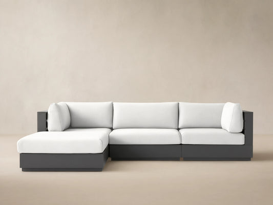 L-shaped Bal Harbour Outdoor Aluminum Four-Piece Sectional with dark gray frame & white cushions, on a stone patio.