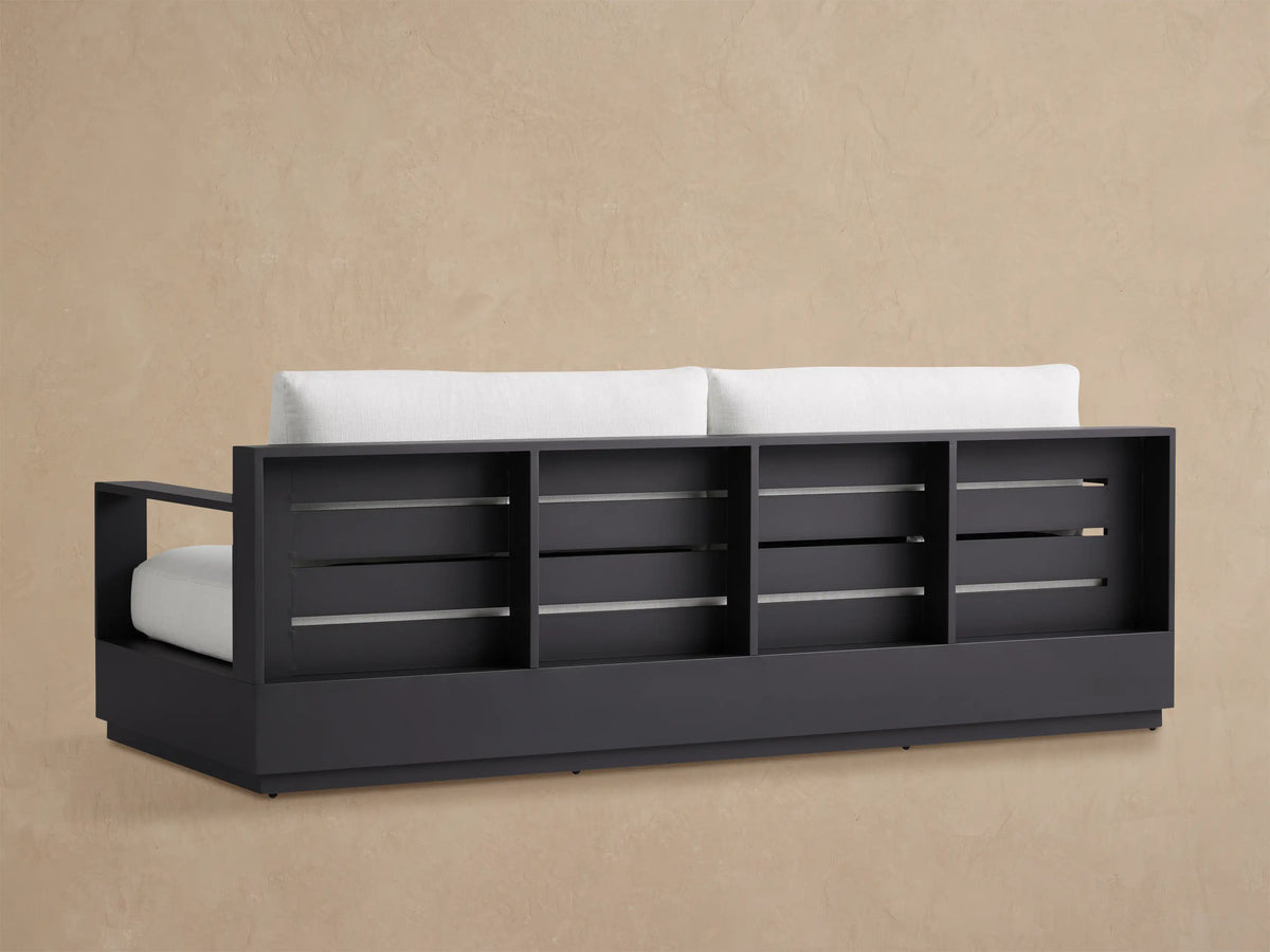 Close-up of Bal Harbour Outdoor Aluminum Sofa's dark gray frame and textured white cushions from an elevated angle.