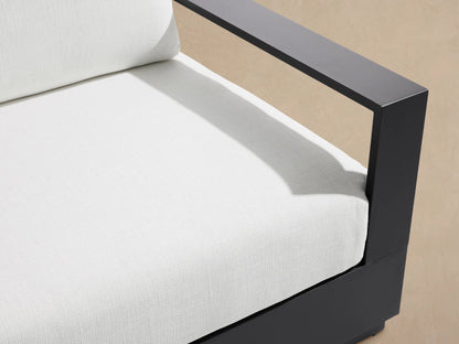 Bal Harbour Outdoor Aluminum Sofa, dark gray frame, white cushions, on a tiled patio with a beige wall background.