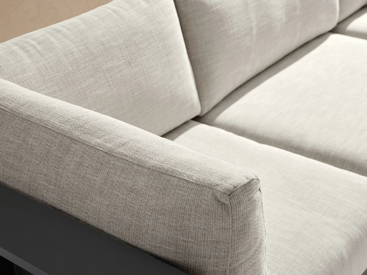 Bal Harbour L-shaped outdoor aluminum sectional with dark gray frame, light beige cushions, and side shelves, on a patio.