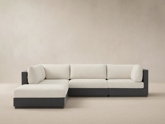 Bal Harbour Outdoor L-shaped sectional with ottoman. Dark gray aluminum frame, light cream cushions on a patterned patio floor.